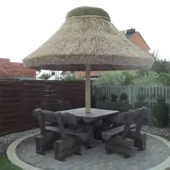 Drewniany stół z ławami pod dużym, słomianym parasolem ogrodowym.