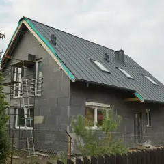 Budowa domu z szarej cegły z szarym dachem, okna dachowe, rusztowanie.
