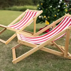 Dwa drewniane leżaki w czerwono-białe pasy na trawie, w tle choinka.