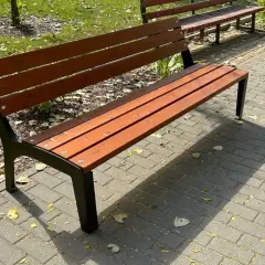 Drewniana ławka ogrodowa z czarnymi metalowymi nogami na wybrukowanym chodniku.