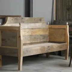 Drewniana ławka ogrodowa z ozdobnymi elementami i krzesło w tle.