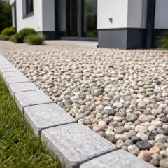 Kamienna opaska wokół domu z żwirowym podjazdem i zielonym trawnikiem.