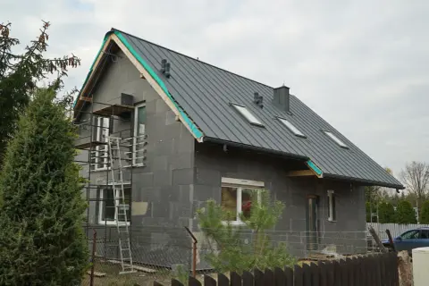 Budowa domu z szarej cegły z szarym dachem, okna dachowe, rusztowanie.