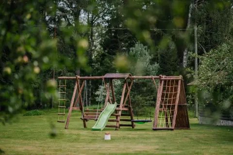 Drewniany plac zabaw z huśtawkami, zjeżdżalnią i ścianką wspinaczkową. Idealne miejsce, by dowiedzieć się, jak zrobić małpi gaj w ogrodzie.