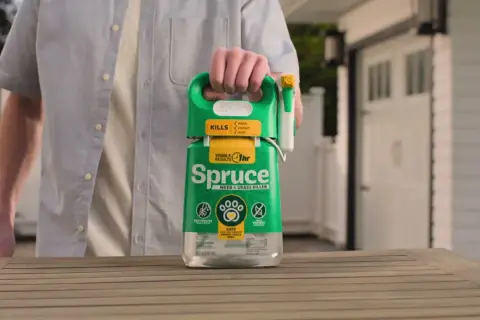 Mężczyzna trzyma butelkę środka "Spruce" - orkan na chwasty. Skutecznie zwalcza chwasty, trawy i mech.