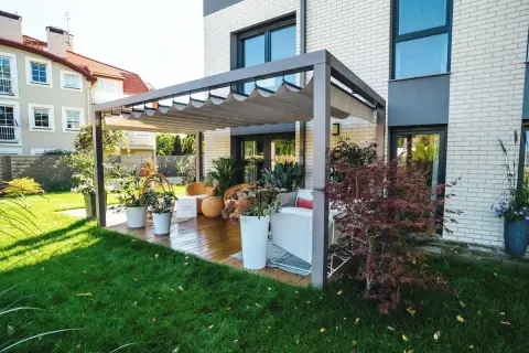 Nowoczesna pergola z wysuwanym dachem na tarasie z drewnianą podłogą i meblami ogrodowymi.