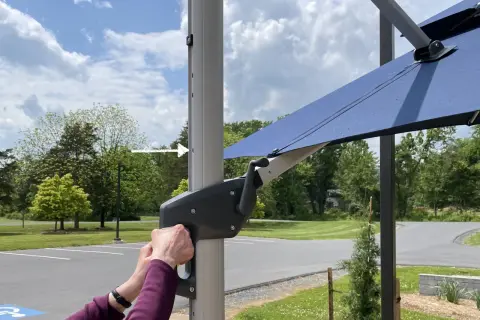 Ręce obracają korbę mechanizmu parasola ogrodowego.