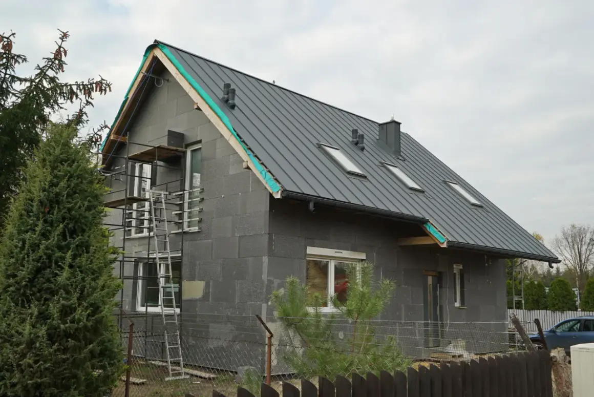 Budowa domu z szarej cegły z szarym dachem, okna dachowe, rusztowanie.