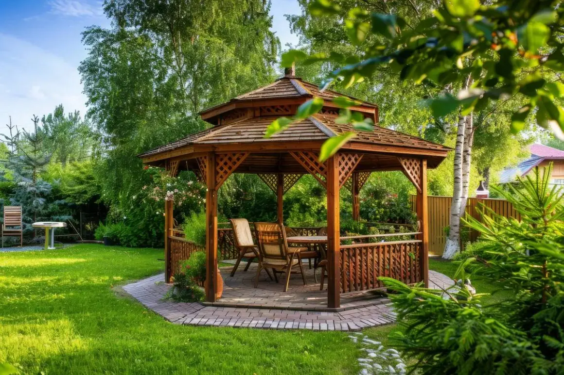Drewniana altana z meblami w ogrodzie, otoczona zielenią.