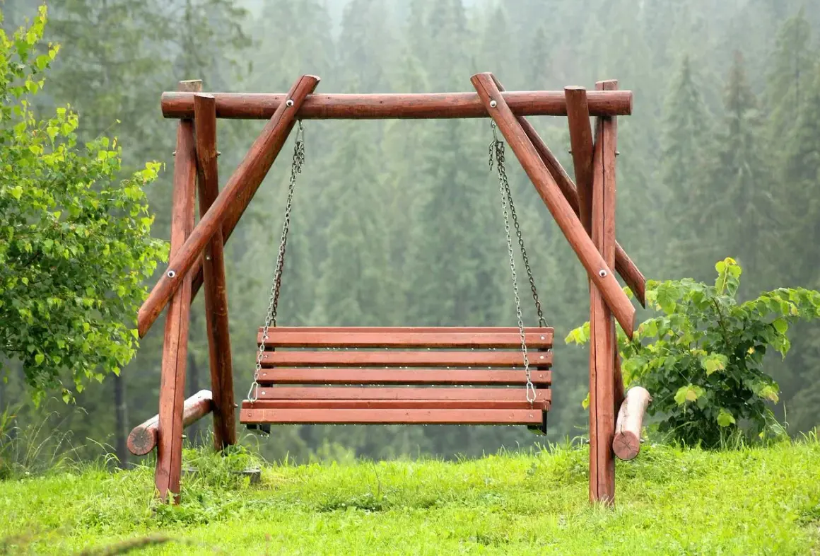 Drewniana huśtawka ogrodowa na tle lasu.