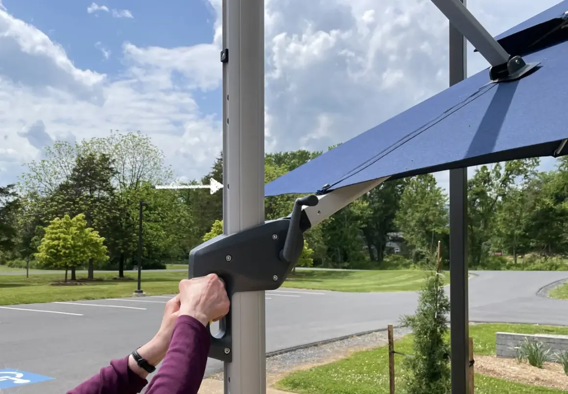 Ręce obracają korbę mechanizmu parasola ogrodowego.