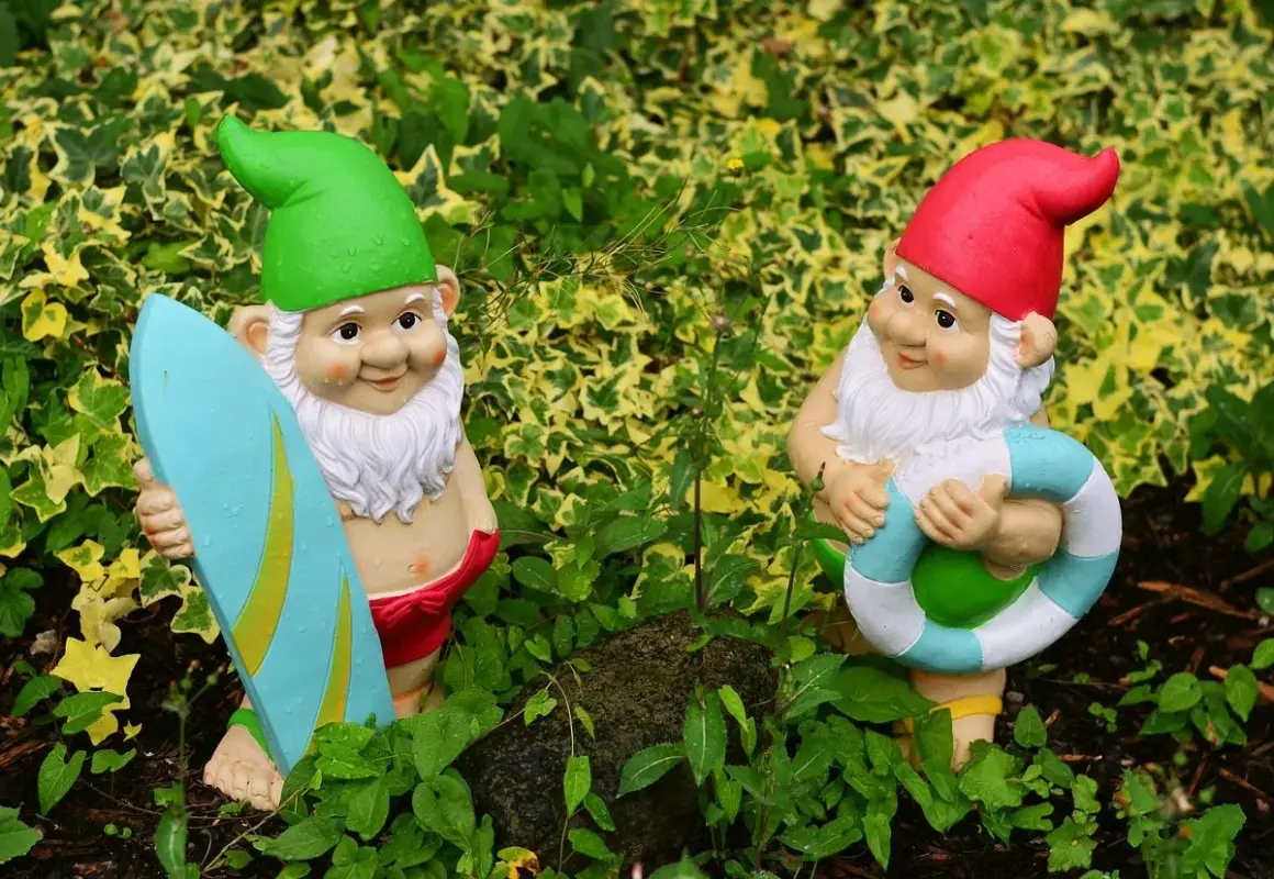 Dwa krasnale ogrodowe, jeden z deską surfingową, drugi z kołem ratunkowym. Idealne do ogrodu, czym pomalować krasnale ogrodowe?