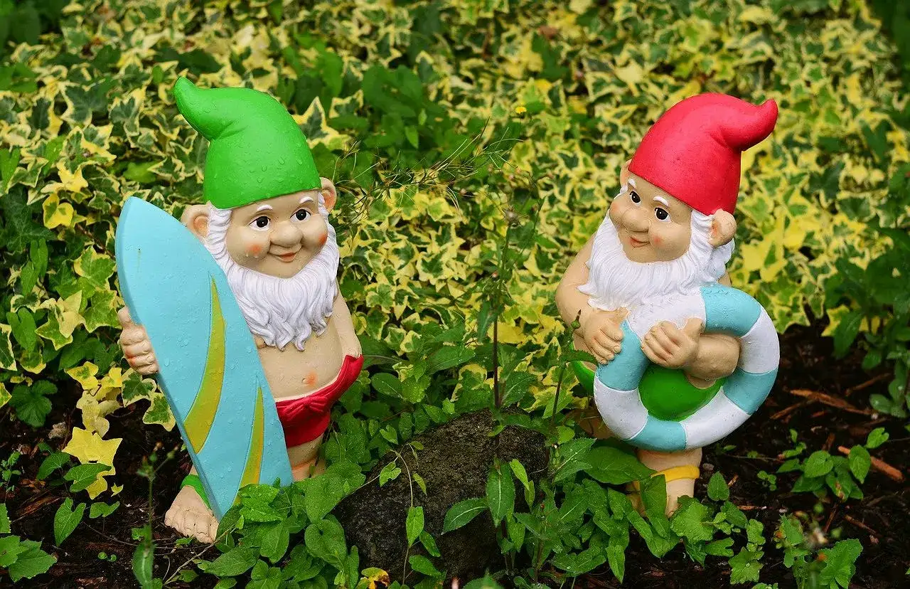 Dwa krasnale ogrodowe, jeden z deską surfingową, drugi z kołem ratunkowym. Idealne do ogrodu, jeśli zastanawiasz się, czym pomalować krasnale ogrodowe.