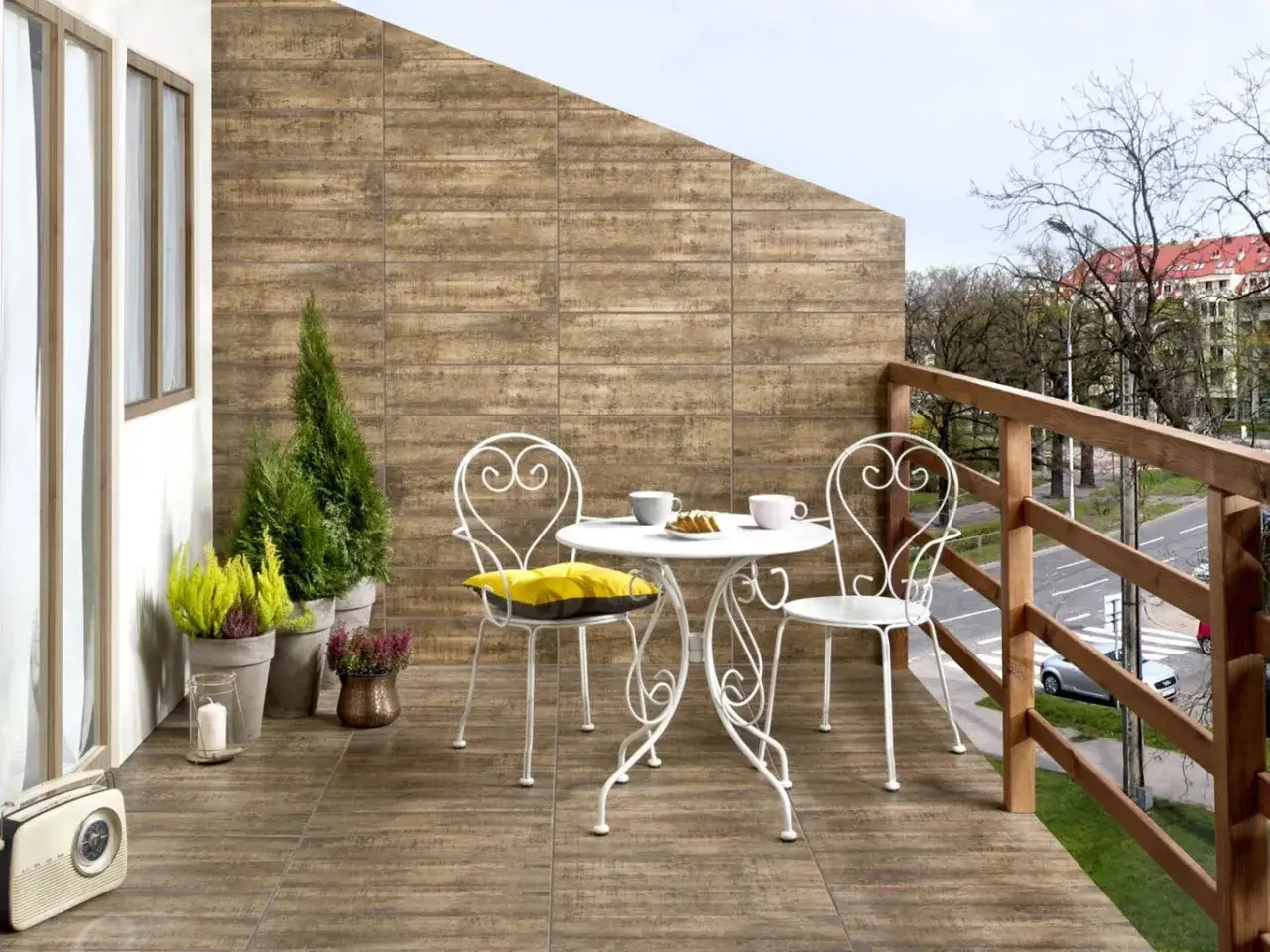 Uroczy balkon z drewnopodobną, tanią podłogą na balkonie, stolikiem i krzesłami, ozdobiony zielenią.