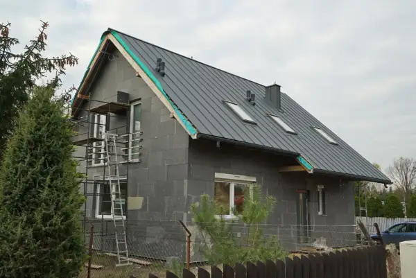 Budowa domu z szarej cegły z szarym dachem, okna dachowe, rusztowanie.