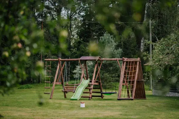 Drewniany plac zabaw z huśtawkami, zjeżdżalnią i ścianką wspinaczkową. Idealne miejsce, by dowiedzieć się, jak zrobić małpi gaj w ogrodzie.