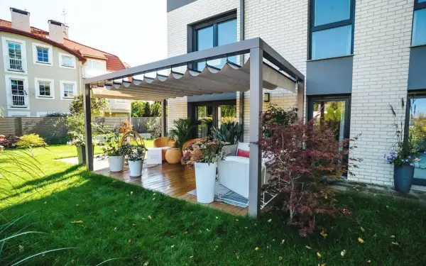 Nowoczesna pergola z wysuwanym dachem na tarasie z drewnianą podłogą i meblami ogrodowymi.