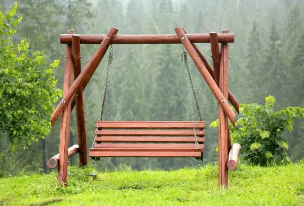 Drewniana huśtawka ogrodowa na tle lasu.