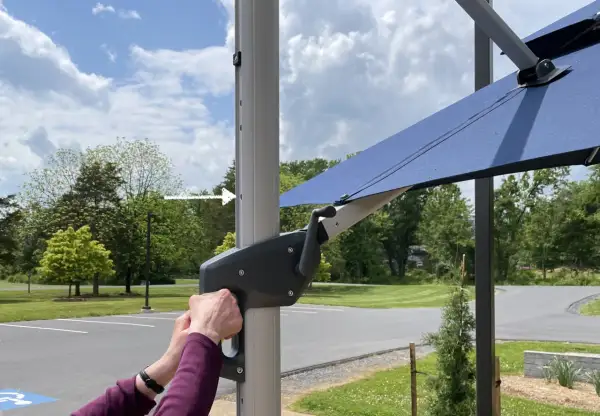 Ręce obracają korbę mechanizmu parasola ogrodowego.