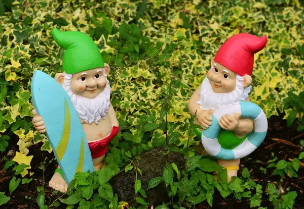 Dwa krasnale ogrodowe, jeden z deską surfingową, drugi z kołem ratunkowym. Idealne do ogrodu, czym pomalować krasnale ogrodowe?